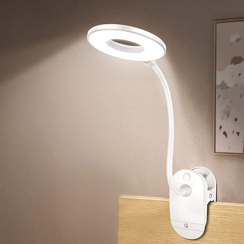 Lampe de lecture blanche à pince, avec bras flexible et tête LED, fixée au bord d’une table en bois.