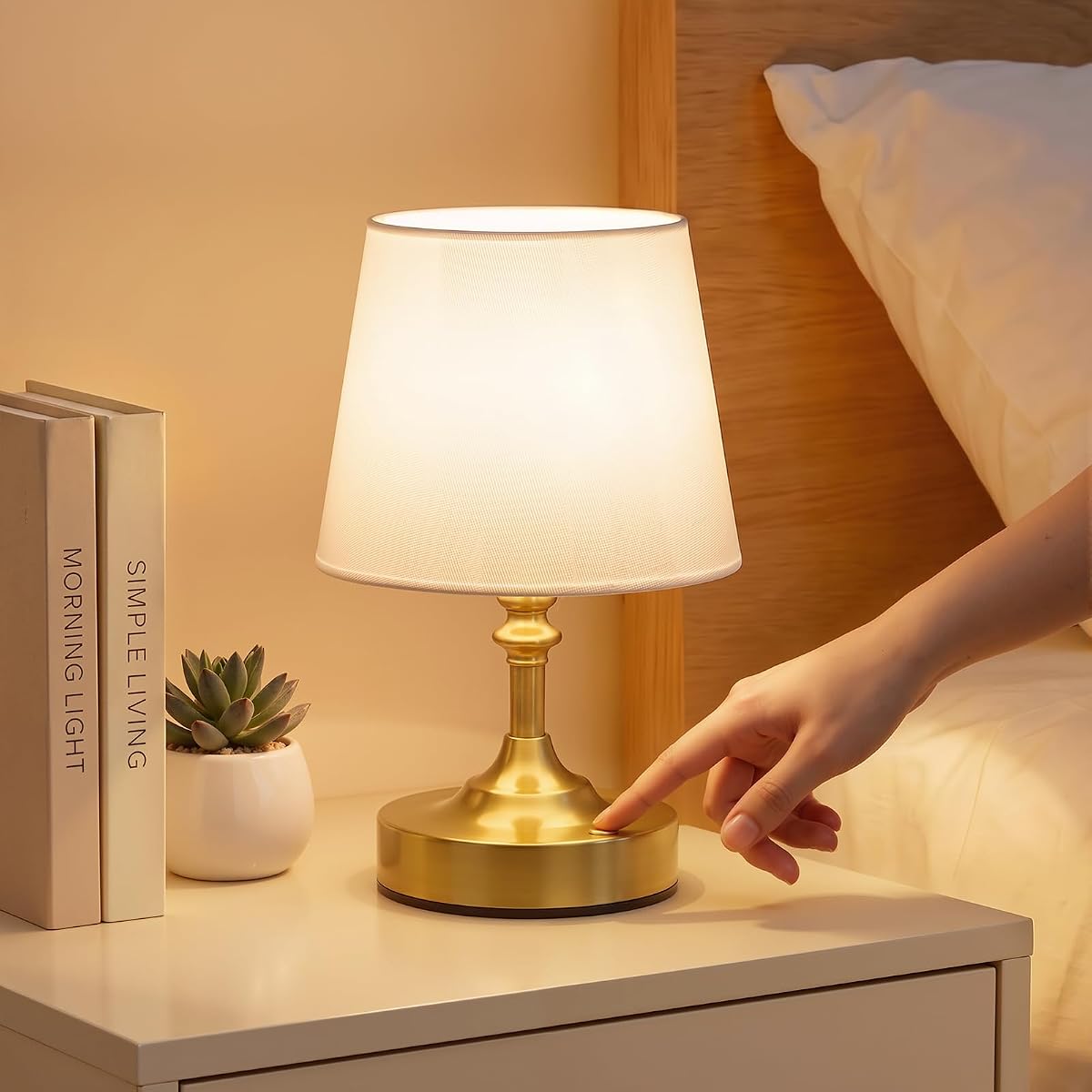 Lampe de chevet sans fil à finition laiton et abat-jour blanc en lin, posée sur une table en bois.