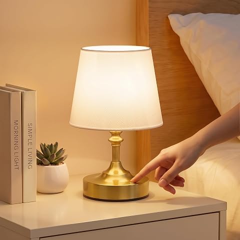 Lampe de chevet sans fil à finition laiton et abat-jour blanc en lin, posée sur une table en bois.